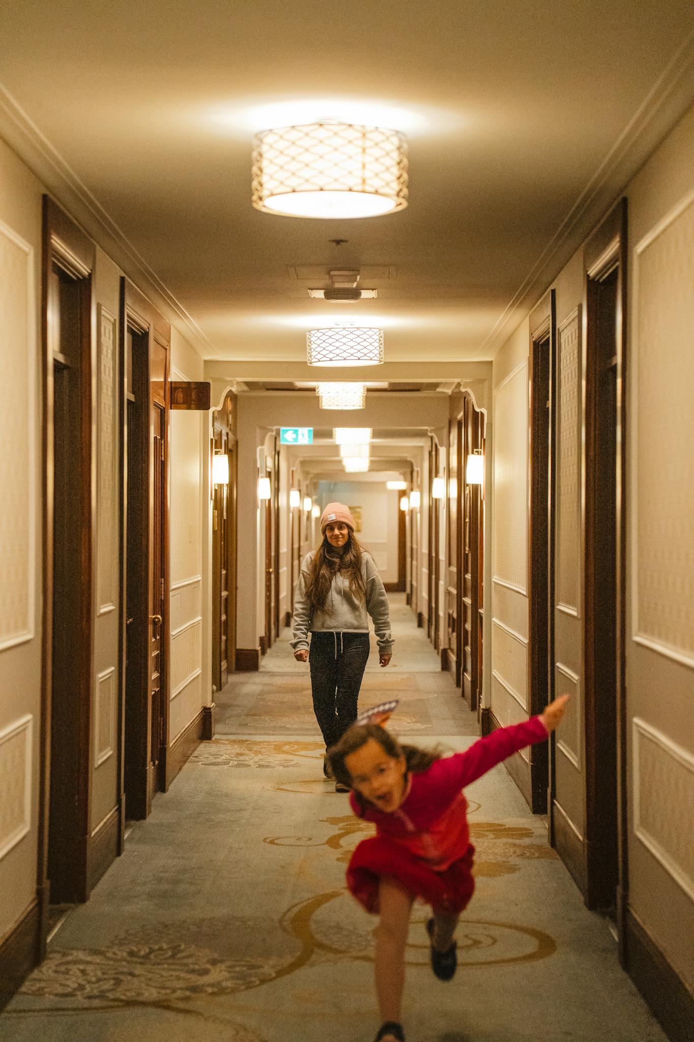 Two children having fun running down a well-lit hotel corridor.